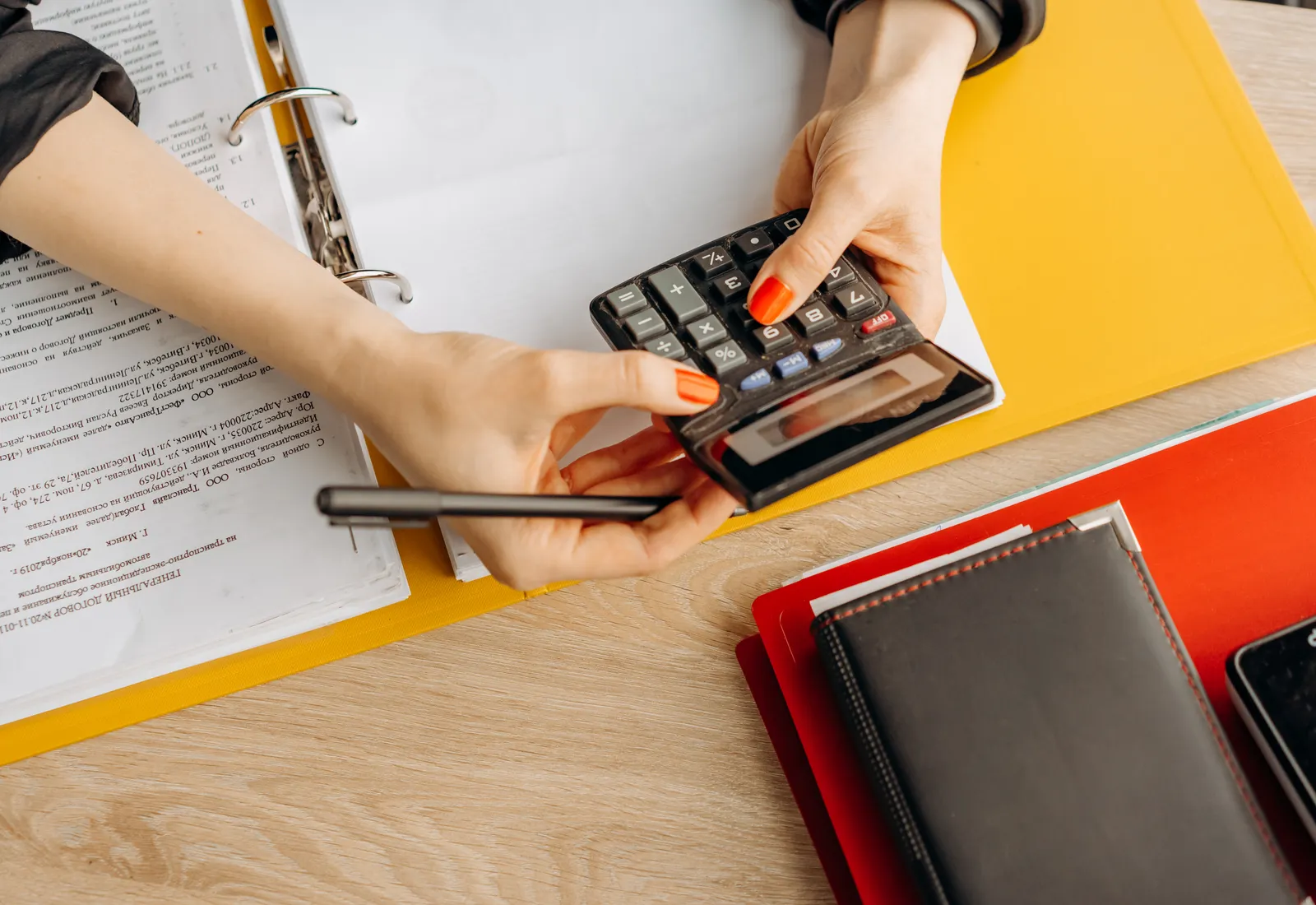 Manos usando una calculadora junto a comprobantes y anotadores